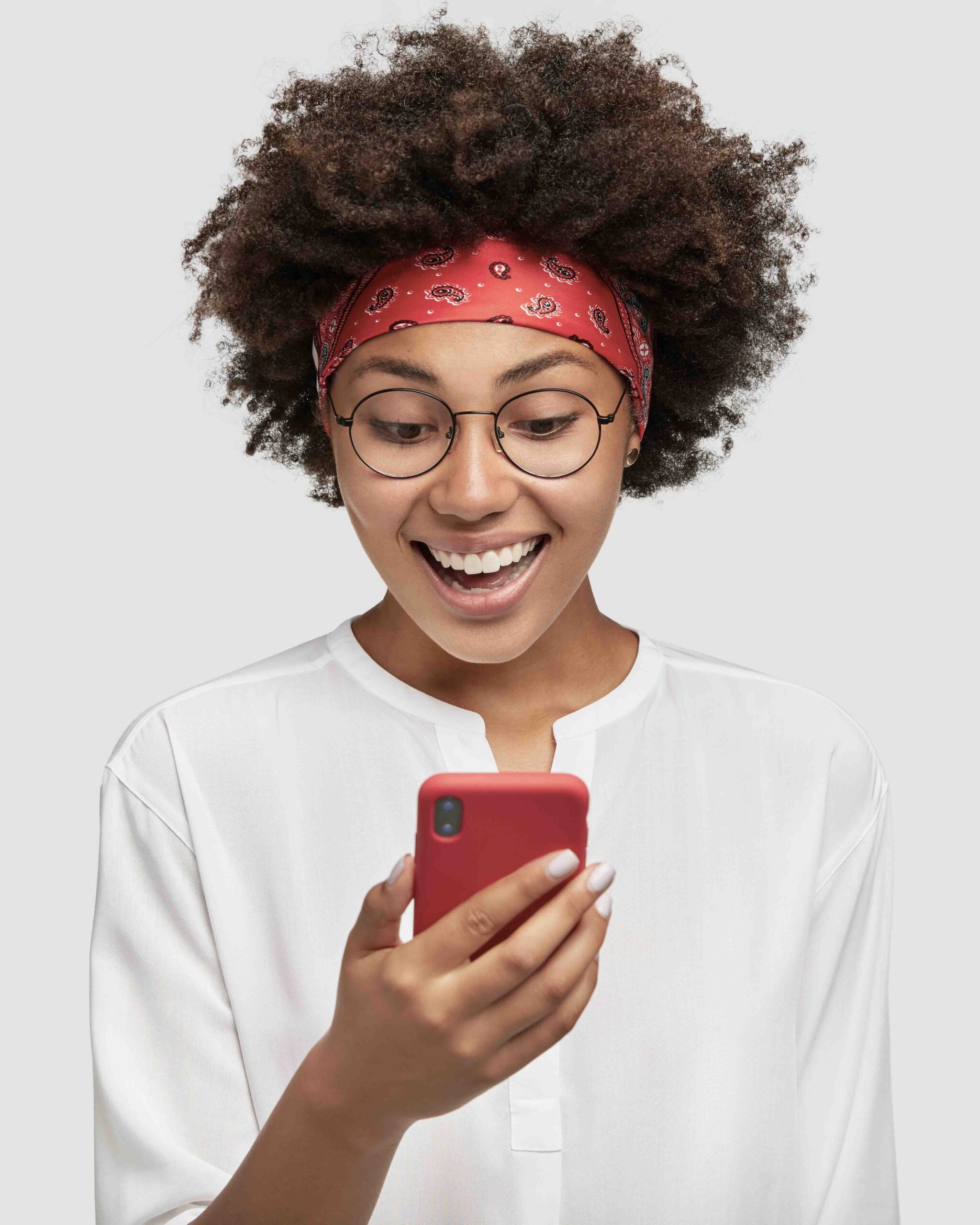 horizontal shot of pleasant looking black adult, excited with video chat, carries up to date cell phone, has broad smile, wears fashionable red headband, models in studio against blank copy space
